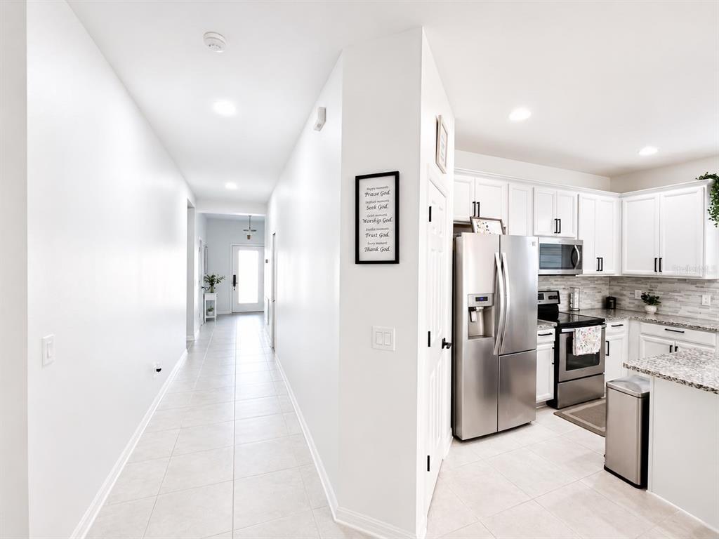 A hallway leads to an entryway next to a kitchen with white cabinets and stainless appliances — 3517 VEGA CREEK DRIVE, ST CLOUD, FL