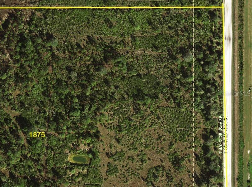 An aerial view shows a wooded plot of land with a small pond and road access — 5151 CHIQUITA DRIVE, PUNTA GORDA, FL