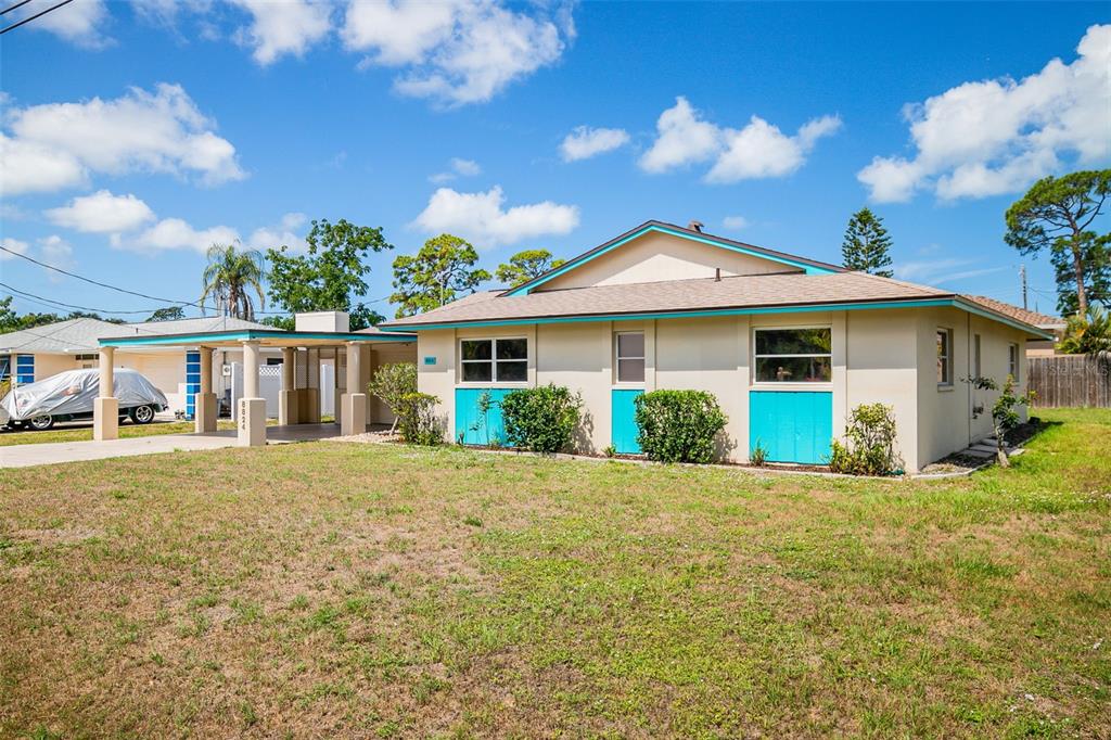 A single-story house with a carport, turquoise accents, and a grassy yard under a blue sky — 8824 PHYLISS AVENUE, SARASOTA, FL