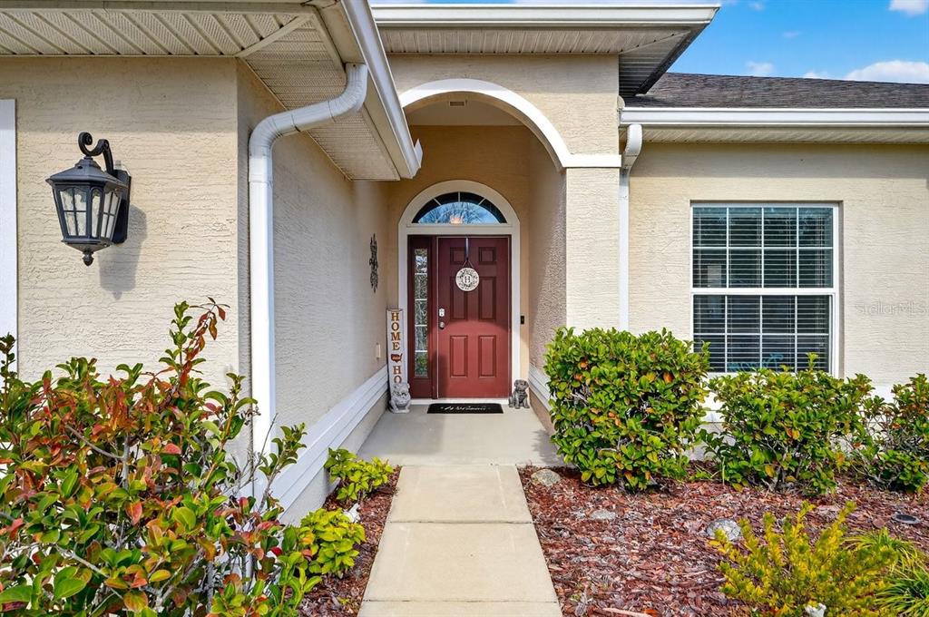 A single-story house with a white garage door, beige stucco exterior, and a red front door — 222 BIRD OF PARADISE DRIVE, PALM COAST, FL