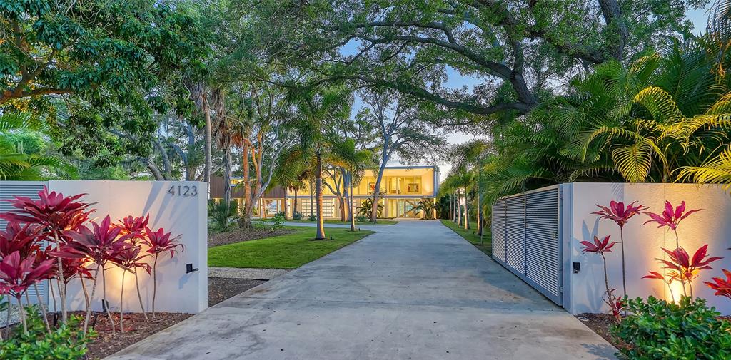 A modern two-story home on stilts features a wood-paneled upper level and glass garage doors — 4123 BAY SHORE ROAD, SARASOTA, FL