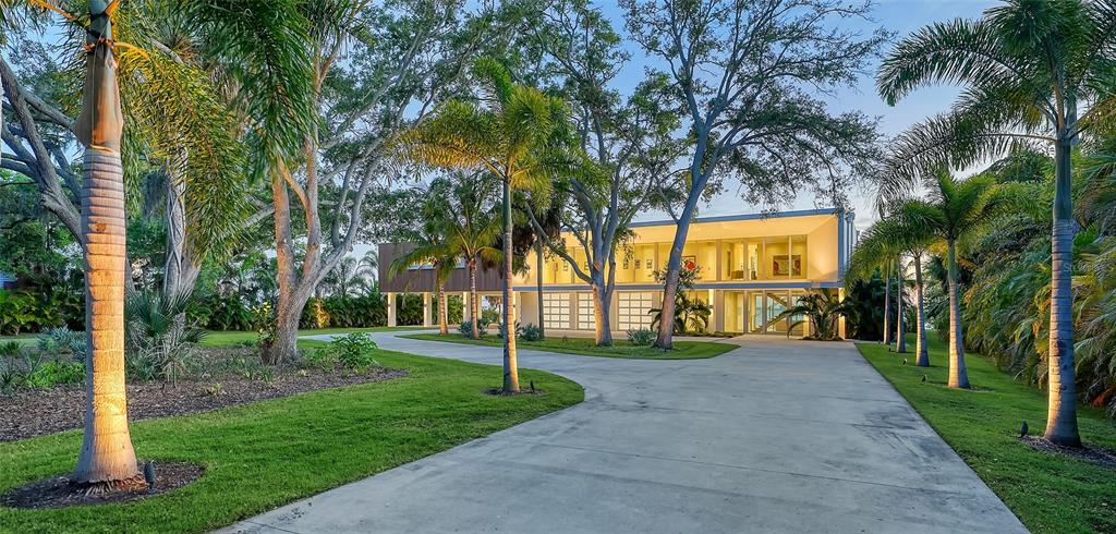 A modern, elevated house with a concrete driveway surrounded by palm trees and mature oaks — 4123 BAY SHORE ROAD, SARASOTA, FL