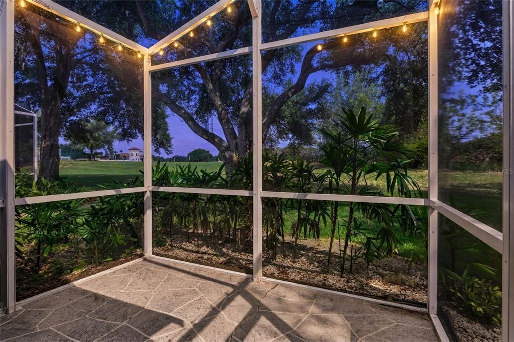 A screened-in patio with stone flooring overlooks a grassy yard with trees and string lights — 26740 CASH COURT, LEESBURG, FL