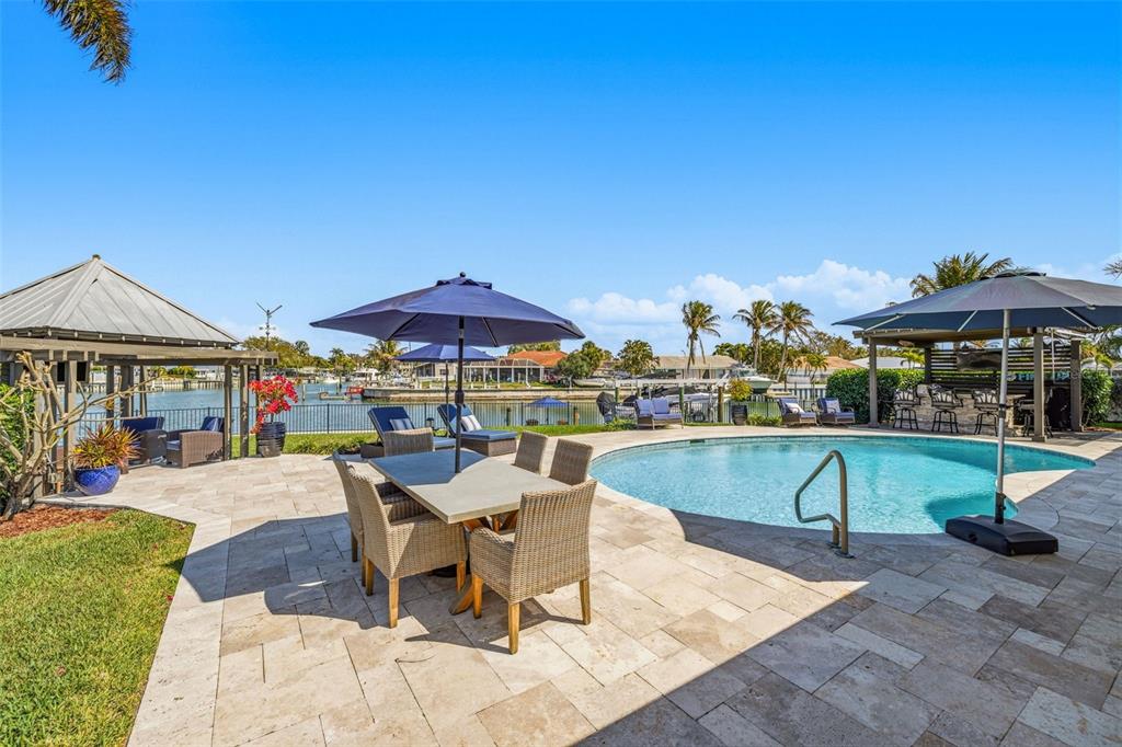 A patio with a dining set, pool, and gazebo overlooks a canal with boats — 4310 40TH STREET S, ST PETERSBURG, FL