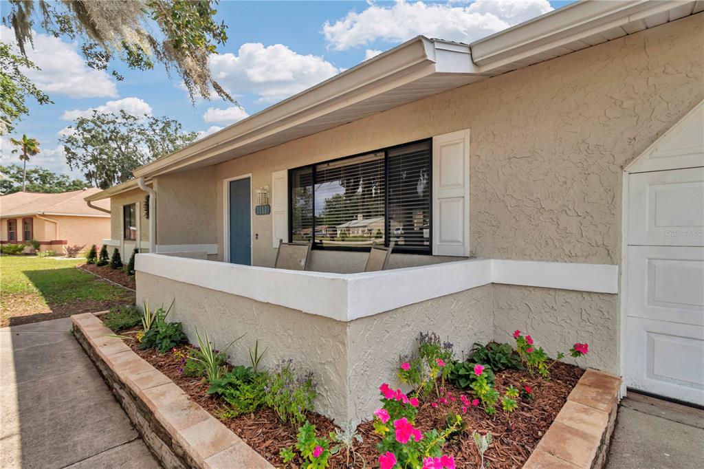 A beige stucco house exterior features a front porch, a window with shutters, and landscaping — 1111 HICKORY ROAD, OCALA, FL