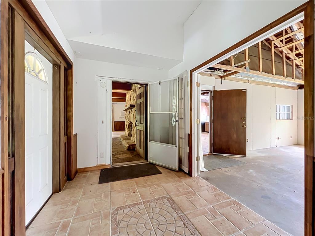 An entryway with tile flooring leads to a stone fireplace and an unfinished garage area — 125 SNOW HILL ROAD, GENEVA, FL