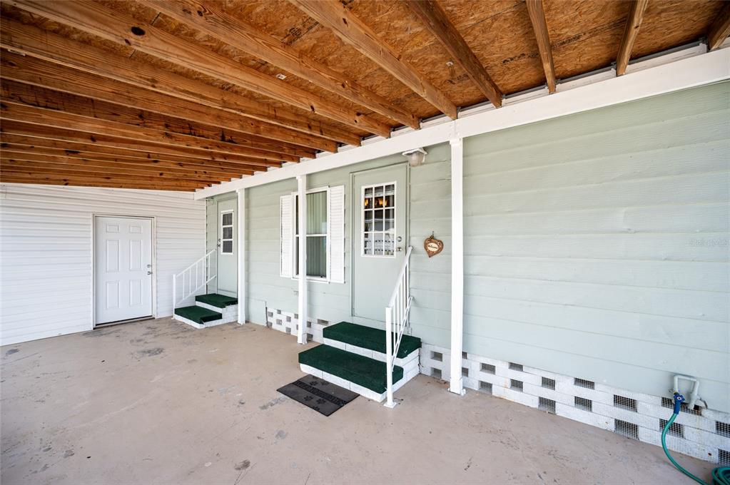 A covered concrete patio features two exterior doors with green steps and light green siding — 6162 REDWING AVENUE, ENGLEWOOD, FL
