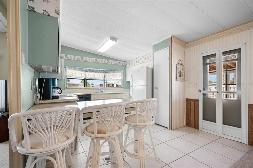 A kitchen features white cabinets, a breakfast bar with wicker stools, and a glass door — 6162 REDWING AVENUE, ENGLEWOOD, FL