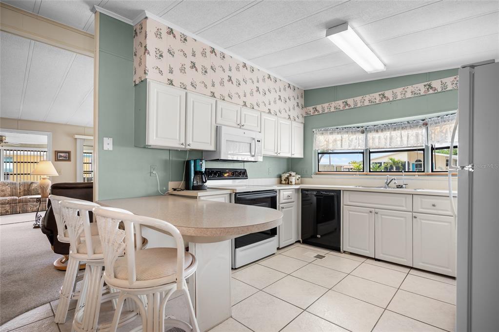 A kitchen with white cabinets, a breakfast bar, tile floors, and floral wallpaper borders — 6162 REDWING AVENUE, ENGLEWOOD, FL