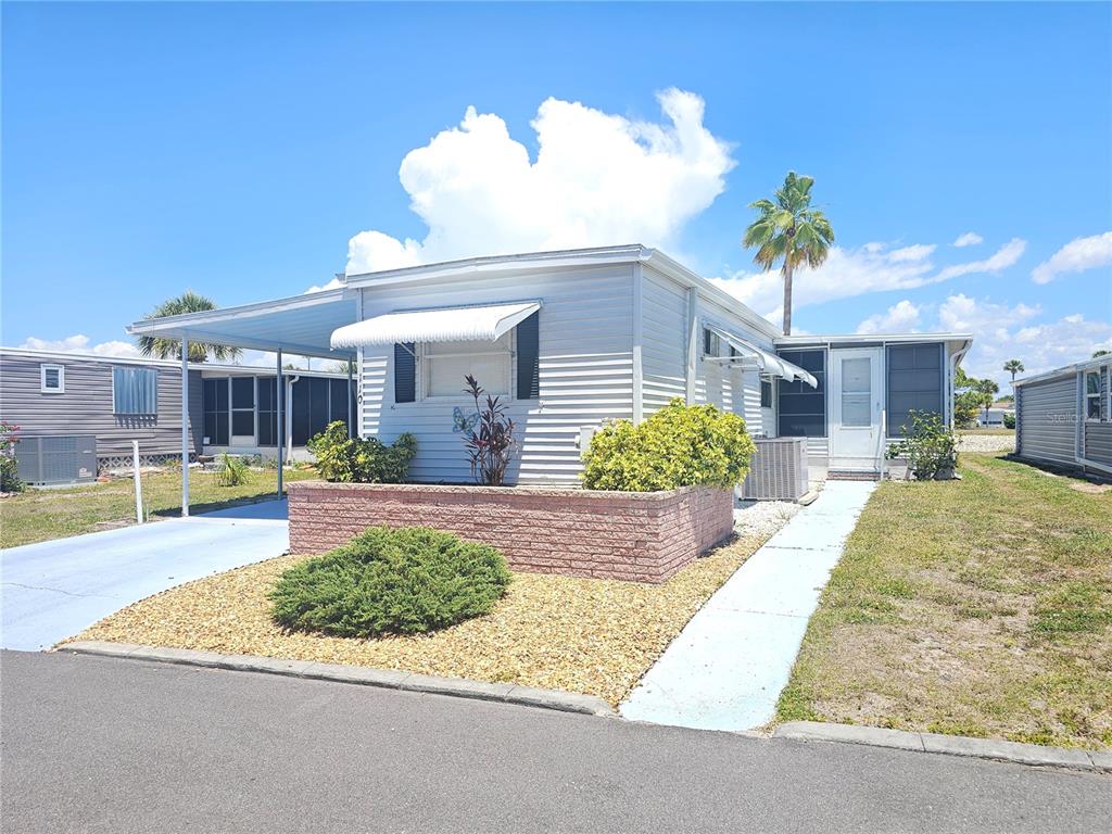 A single-story manufactured home features a brick planter, a carport, and a gravel front yard — 110 ROMA ROAD, VENICE, FL