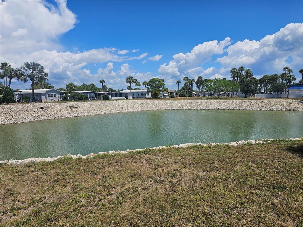 A pond with a rock-lined bank sits in front of several manufactured homes and trees — 110 ROMA ROAD, VENICE, FL