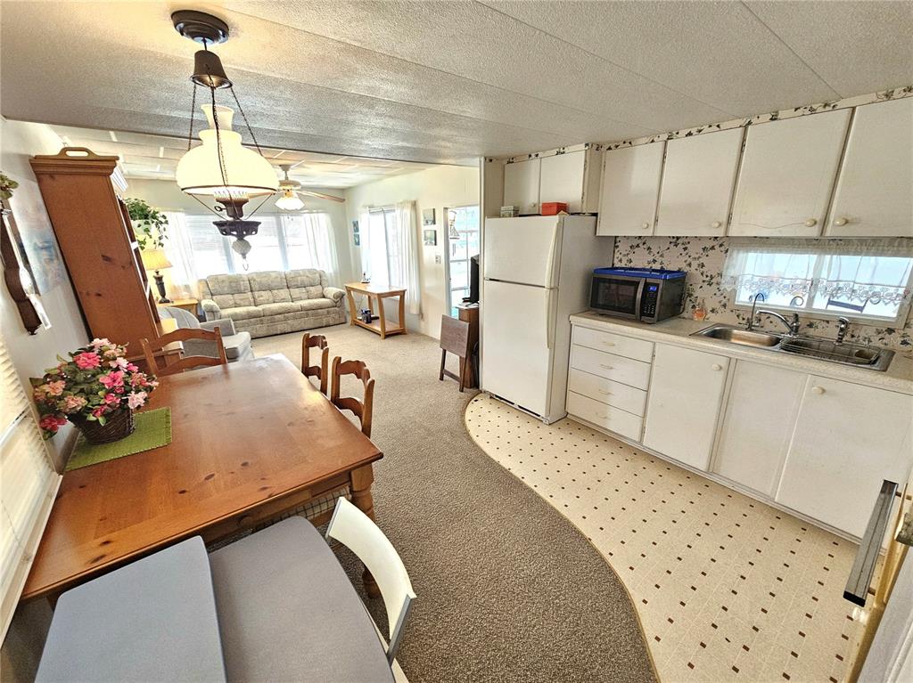An open-concept kitchen and dining area features white cabinets, vinyl flooring, and carpeted living space — 110 ROMA ROAD, VENICE, FL
