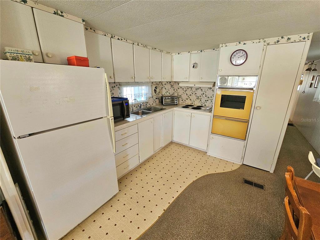 A kitchen features white cabinets, a white refrigerator, a wall oven, and patterned wallpaper — 110 ROMA ROAD, VENICE, FL