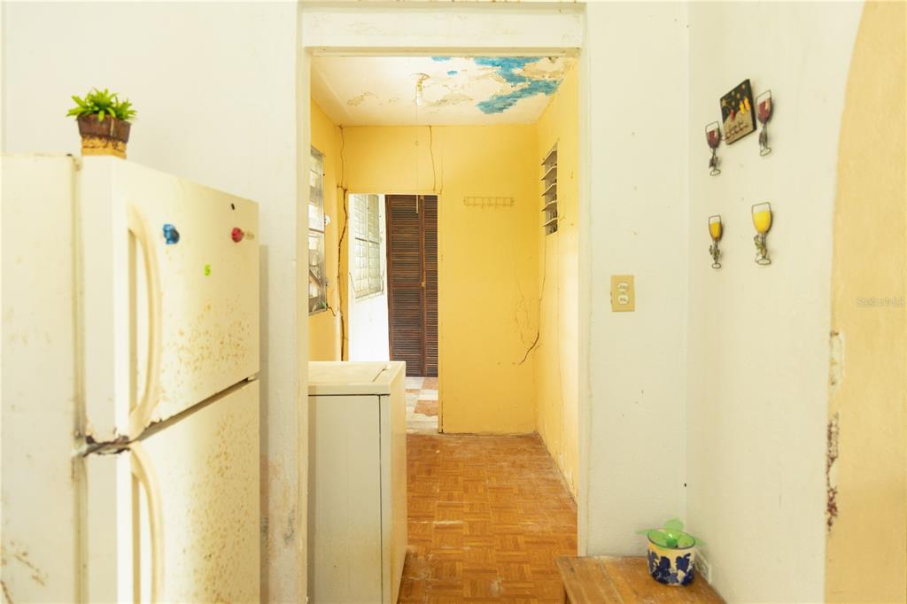 A kitchen with a white refrigerator, yellow walls, and a damaged ceiling leads to another room — 16 CALLE SCORPIO, VIEQUES, PR