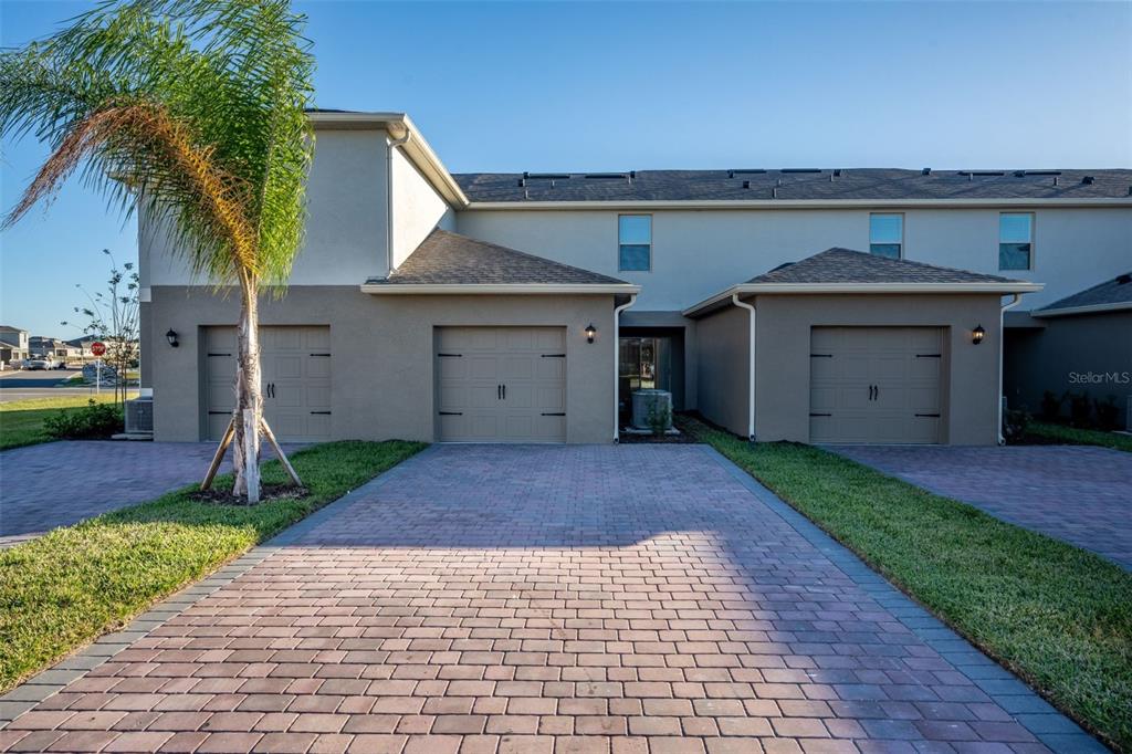A two-story townhouse exterior features three garage doors and a paved driveway — 13453 SAGESTONE DRIVE, WINTER GARDEN, FL
