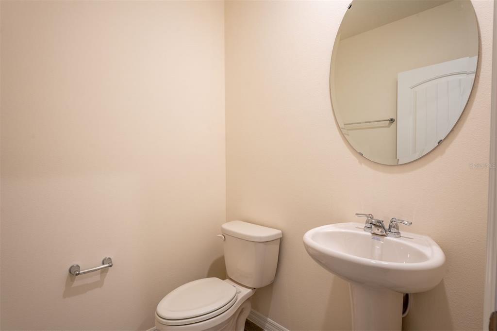 A half bathroom features a pedestal sink, a round mirror, and a white toilet — 13453 SAGESTONE DRIVE, WINTER GARDEN, FL