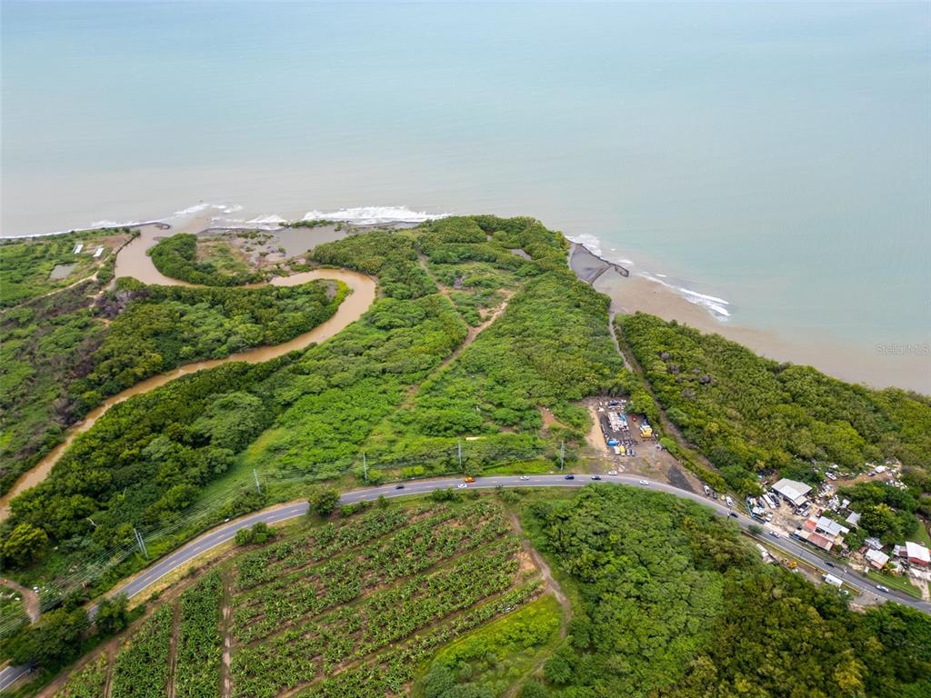 An aerial view shows a coastal landscape with a winding river, dense vegetation, and a road — PR-1 PUEBLO WARD, SALINAS, PR