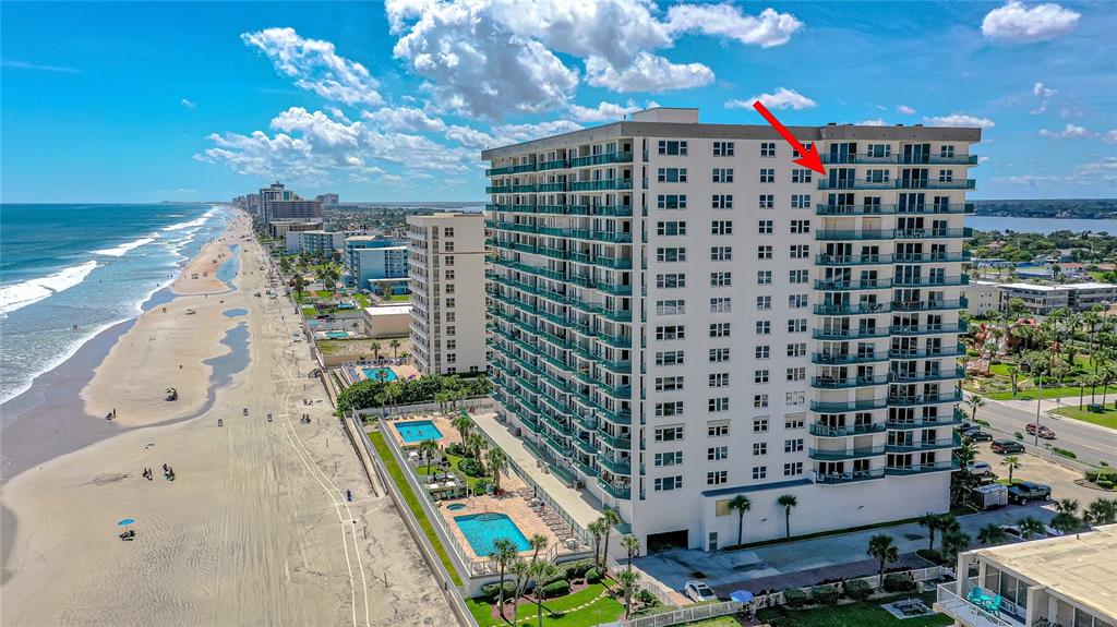 An aerial view shows a tall beachfront condominium building with a red arrow pointing toward a balcony — 2055 S ATLANTIC AVENUE UNIT 1402, DAYTONA BEACH, FL