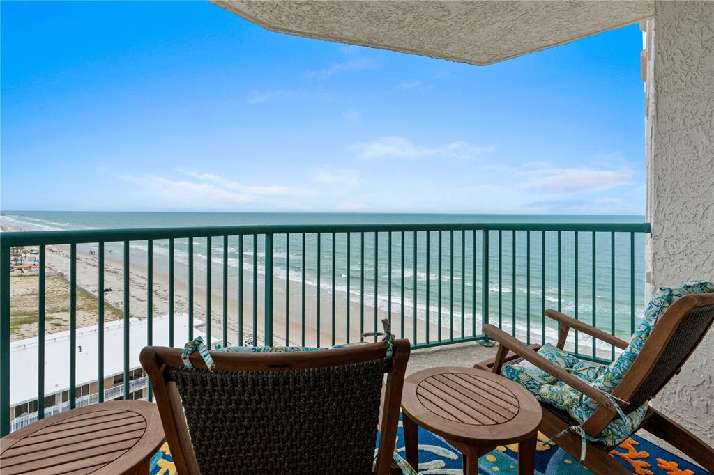 A balcony with two wooden chairs and small tables overlooks the ocean and beach — 2055 S ATLANTIC AVENUE UNIT 1402, DAYTONA BEACH, FL