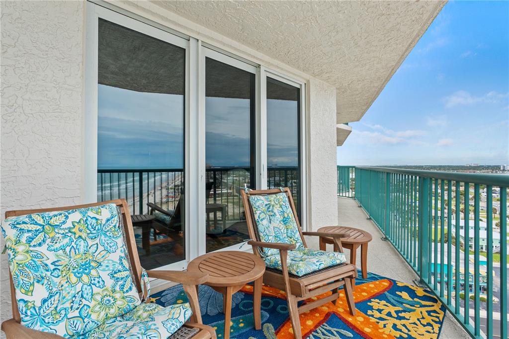 A balcony features two wooden chairs, small tables, and a colorful rug overlooking the ocean — 2055 S ATLANTIC AVENUE UNIT 1402, DAYTONA BEACH, FL