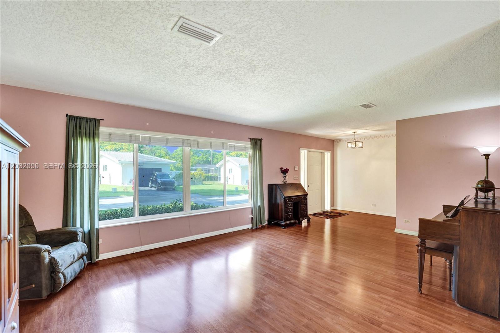 A living room with pink walls, wood flooring, a large window, and a piano — 7421 NW 8th Ct, Plantation FL 33317, PLANTATION, FL