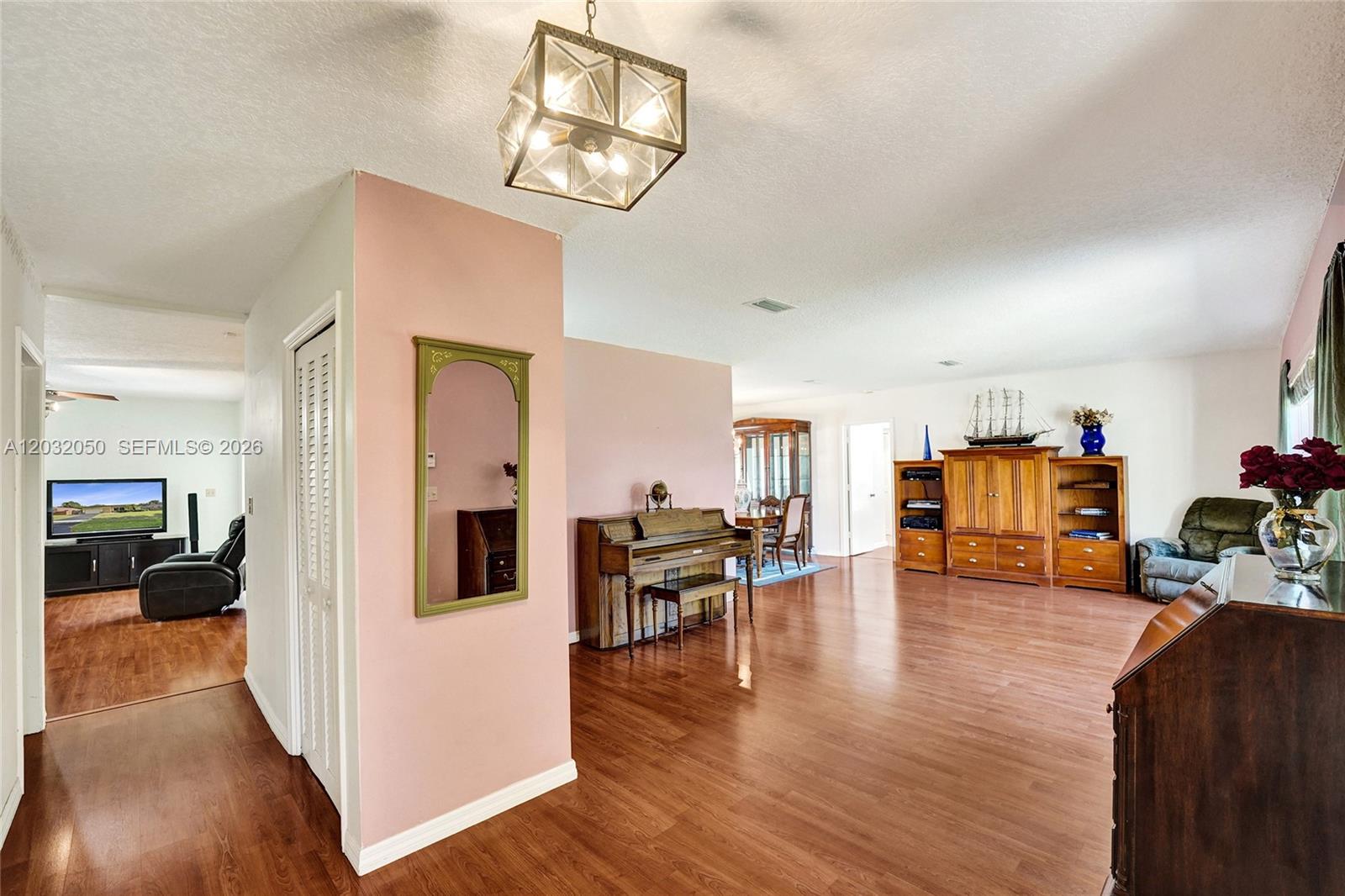 A living room features wood-look flooring, a piano, a large wooden entertainment center, and pink walls — 7421 NW 8th Ct, Plantation FL 33317, PLANTATION, FL