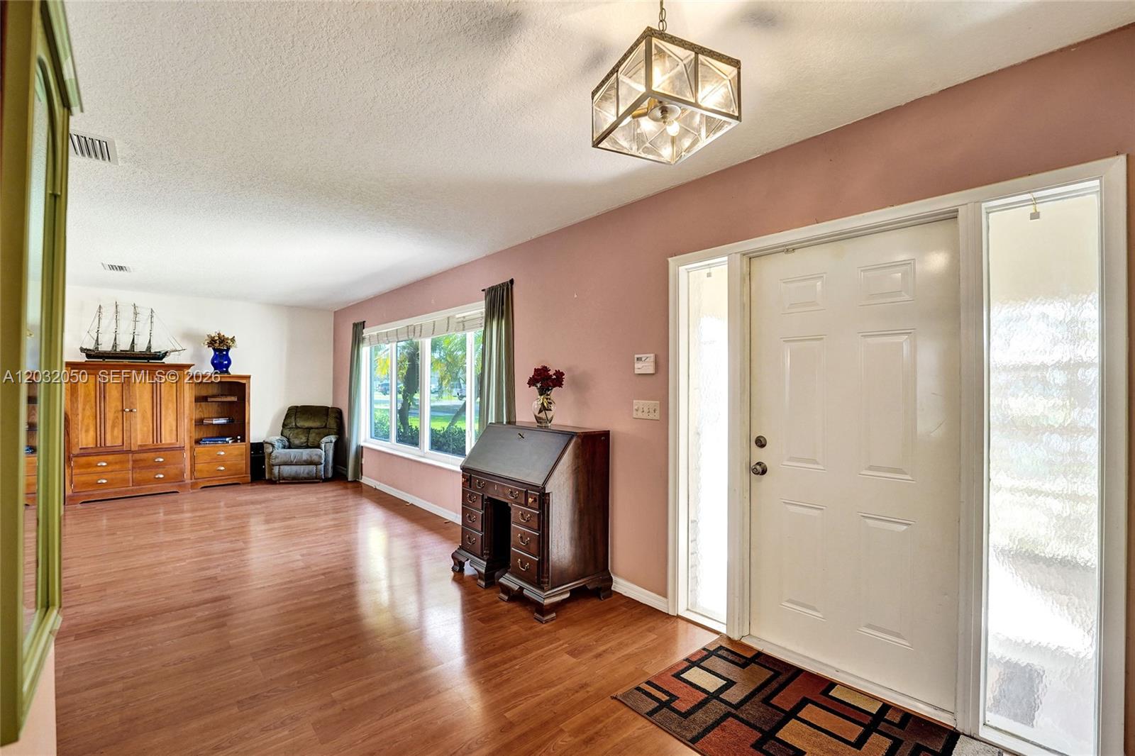 A living room features light wood flooring, pink walls, a white front door, and furniture — 7421 NW 8th Ct, Plantation FL 33317, PLANTATION, FL