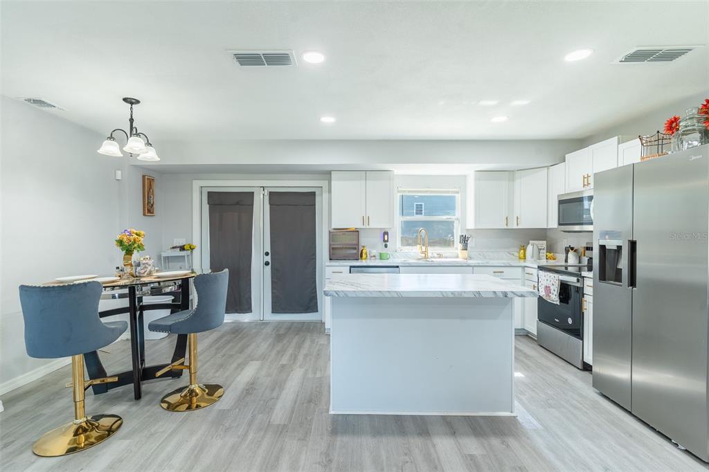 A kitchen with white cabinets, a marble-topped island, stainless steel appliances, and a dining area — 713 GREENLEAF LANE, LAKE WALES, FL