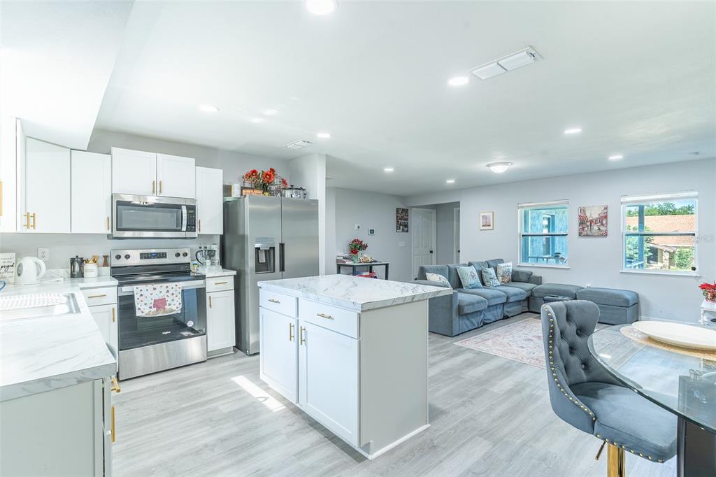 An open-concept kitchen with white cabinets and a marble-topped island overlooks a living area — 713 GREENLEAF LANE, LAKE WALES, FL