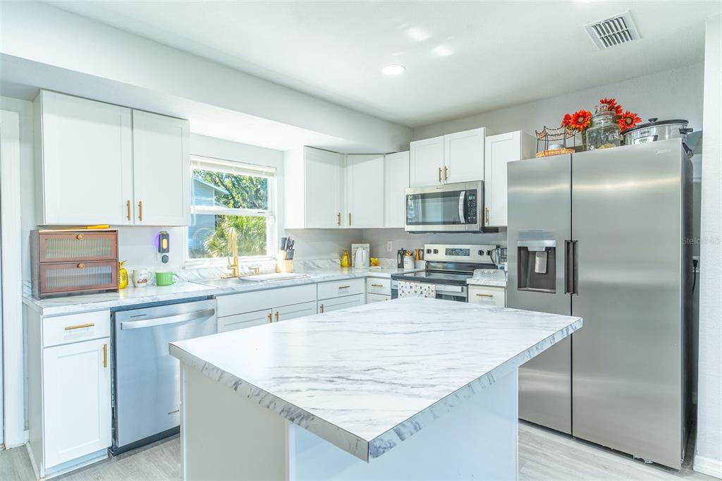 A kitchen features white cabinets, stainless steel appliances, and a marble-patterned island countertop — 713 GREENLEAF LANE, LAKE WALES, FL