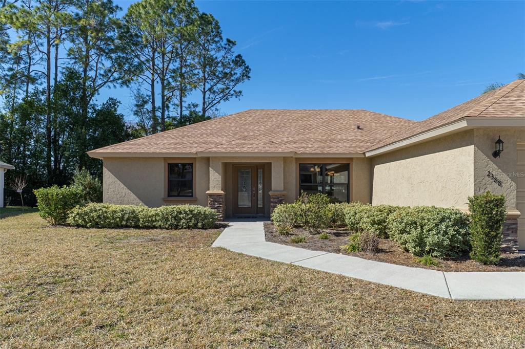 A single-story house with a tan stucco exterior, brown shingled roof, and a concrete walkway — 2388 N BRENTWOOD CIRCLE, LECANTO, FL