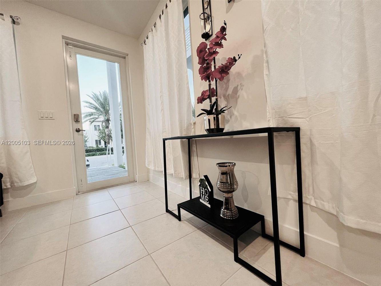 A modern entryway features white tile floors, a black console table, and a glass door — 10300 NW 66TH AV # 101, Doral FL 33178, DORAL, FL