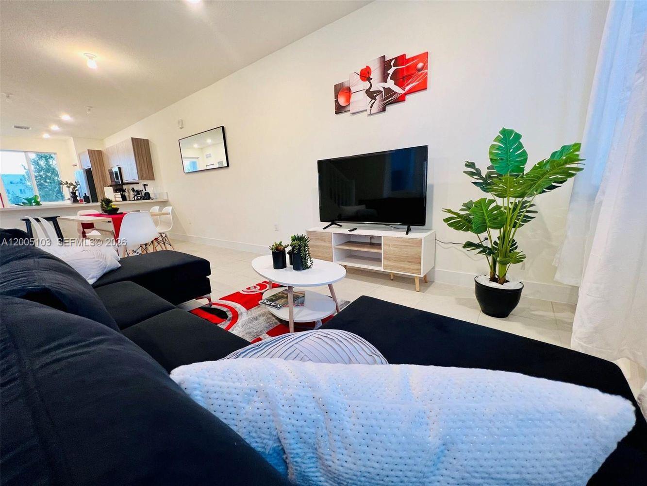 A living room features a black sectional sofa, a television on a stand, and a plant — 10300 NW 66TH AV # 101, Doral FL 33178, DORAL, FL