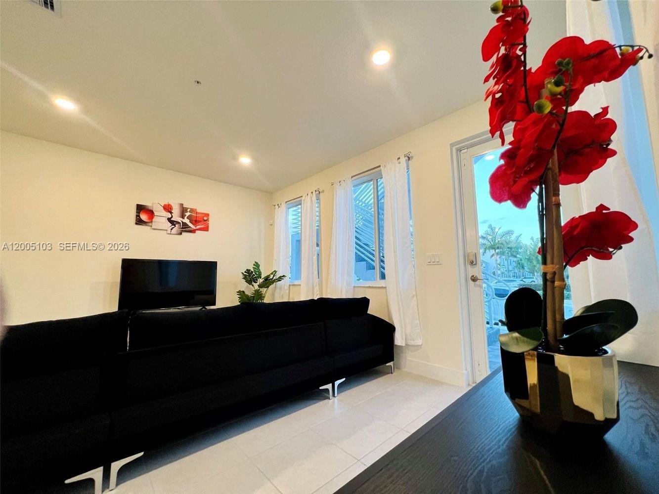 A living room features a black sofa, a television, and a red floral arrangement — 10300 NW 66TH AV # 101, Doral FL 33178, DORAL, FL