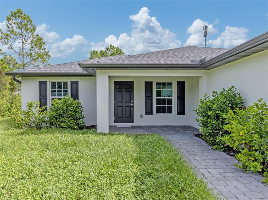 A white house exterior features a black front door, dark shutters, and a stone walkway — 22444 DONALDA AVENUE, PORT CHARLOTTE, FL