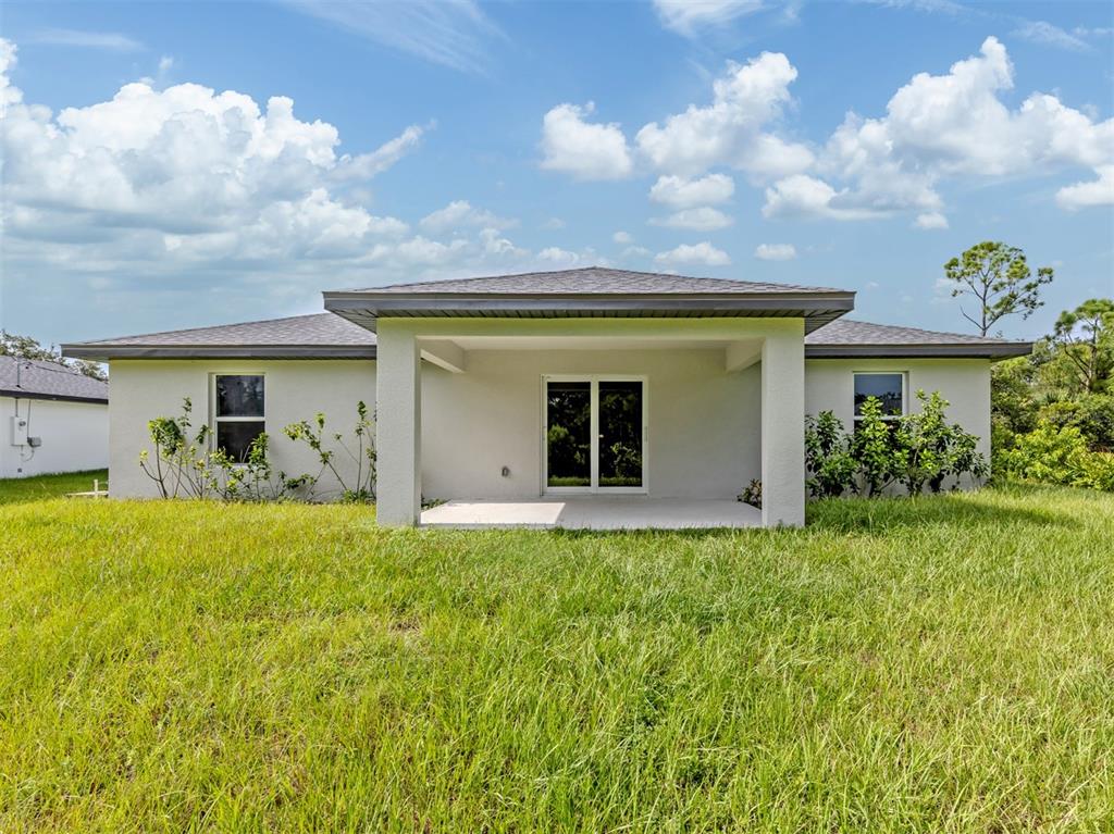 The back exterior of a single-story house features a covered patio and a grassy yard — 22444 DONALDA AVENUE, PORT CHARLOTTE, FL