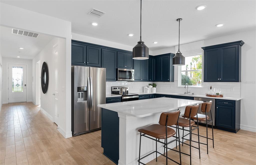 A modern kitchen features dark blue cabinets, a white island with bar stools, and stainless appliances — 2641 FERMOY DRIVE, ORMOND BEACH, FL