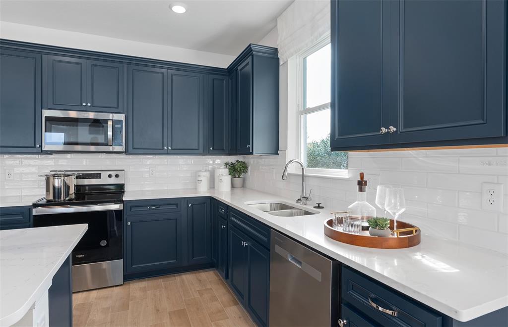 A kitchen features dark blue cabinets, white countertops, a subway tile backsplash, and stainless appliances — 2641 FERMOY DRIVE, ORMOND BEACH, FL