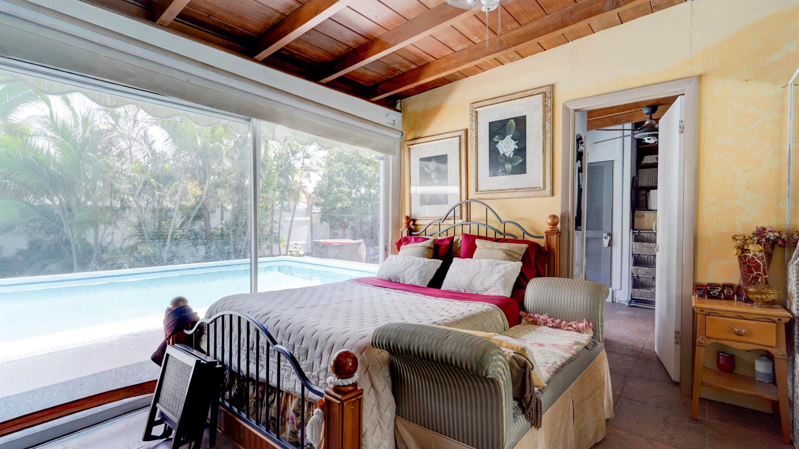 A bedroom features a metal bed frame, wood-beamed ceiling, and sliding doors overlooking a pool — 3246 Orange Street, Boynton Beach FL 33435, BOYNTON BEACH, FL