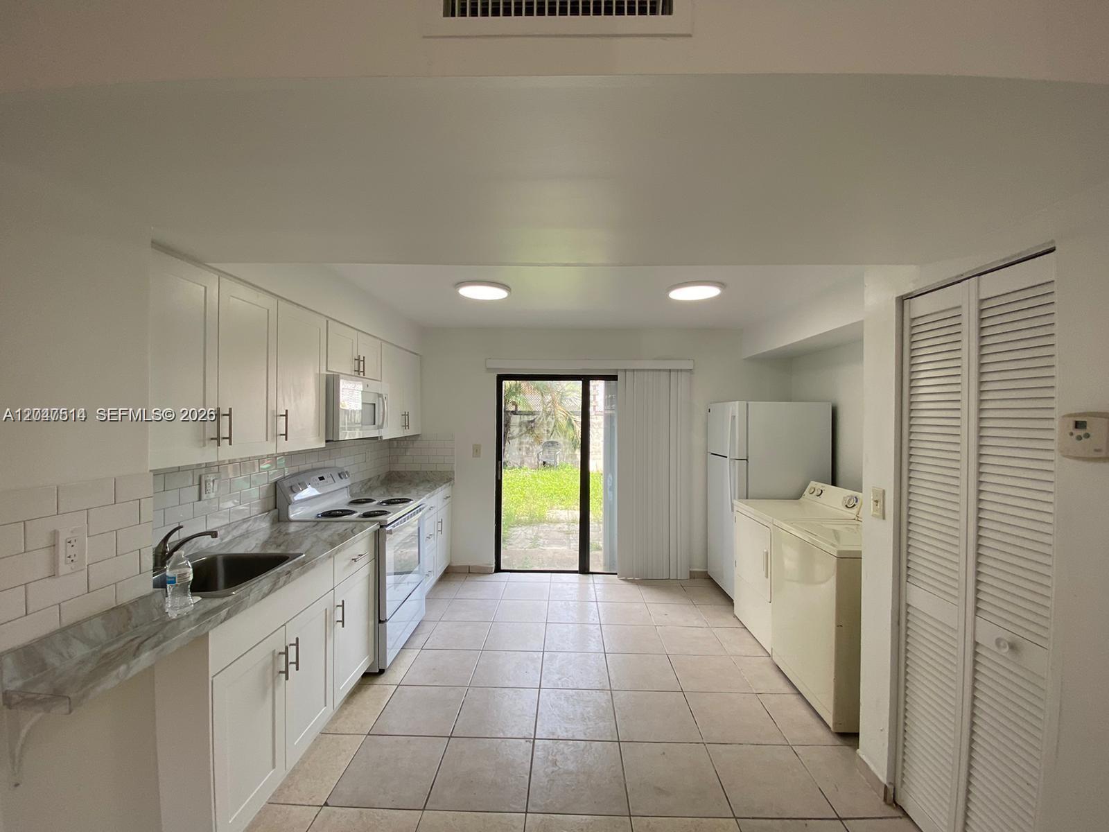 A kitchen features white cabinets, light countertops, tile flooring, and a sliding glass door — 61 NW 132nd Pl # 0, Miami FL 33182, MIAMI, FL