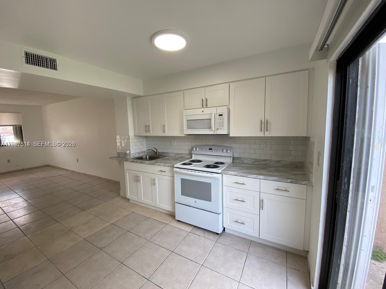 A kitchen features white cabinets, a white stove, and a marble-patterned countertop — 61 NW 132nd Pl # 0, Miami FL 33182, MIAMI, FL