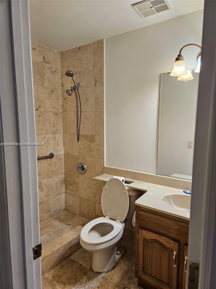 A bathroom features a tiled walk-in shower, a toilet, and a wooden vanity with a mirror — 61 NW 132nd Pl # 0, Miami FL 33182, MIAMI, FL