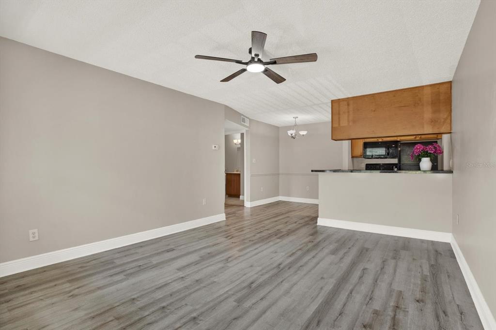 A living room with gray wood-look flooring, a ceiling fan, and an open kitchen pass-through — 308 LAKE PARSONS GREEN UNIT 203, BRANDON, FL