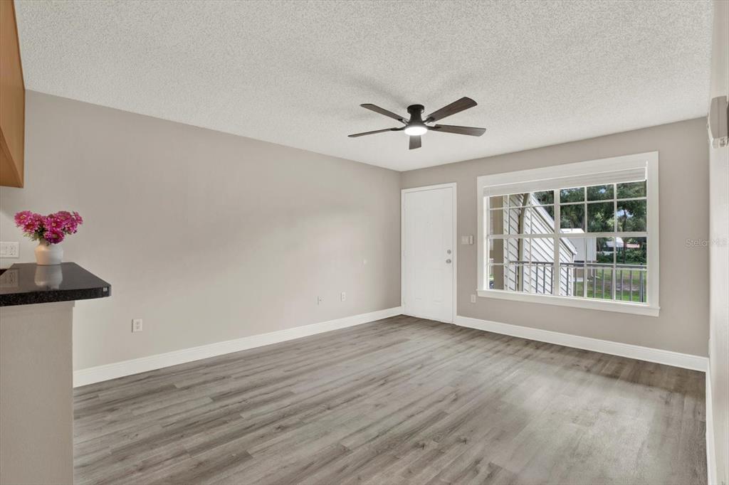 An empty room features gray wood-look flooring, light walls, a ceiling fan, and a window — 308 LAKE PARSONS GREEN UNIT 203, BRANDON, FL