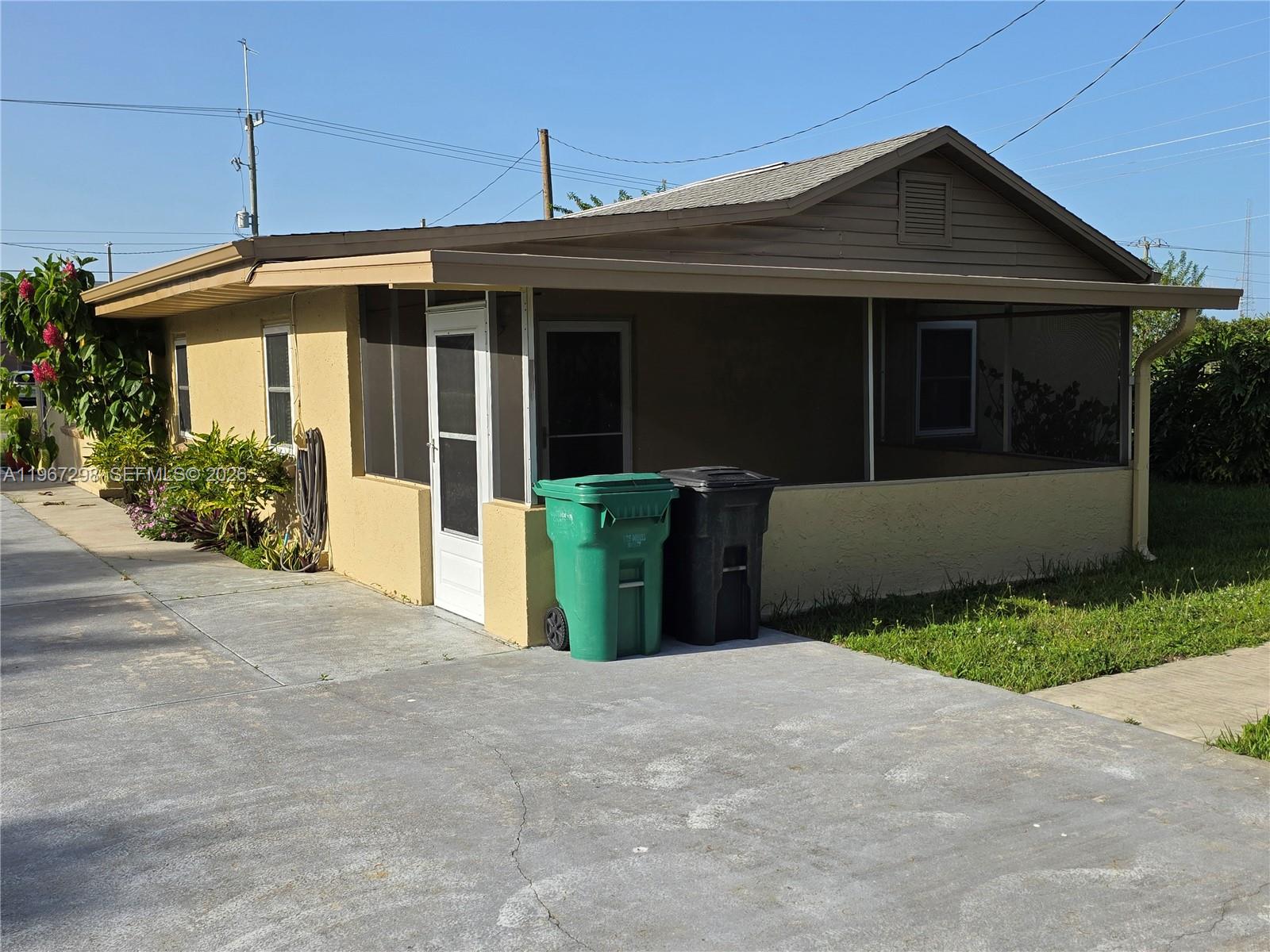 A single-story house with a screened-in porch, yellow stucco walls, and two trash bins outside — 4321 Kirby Loop Rd # 1, Fort Pierce FL 34981, FORT PIERCE, FL
