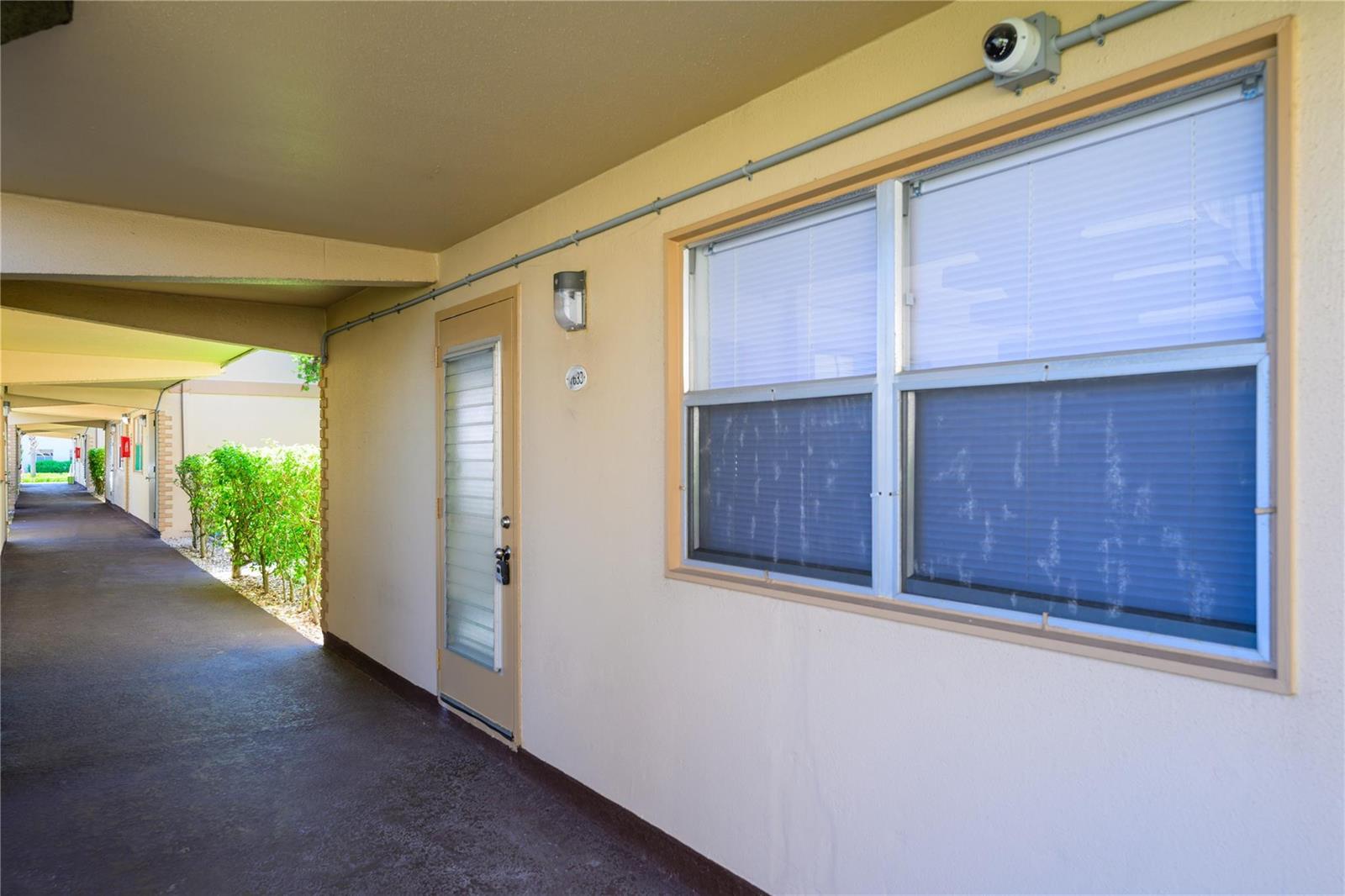 An exterior view of a building walkway featuring a door, window, and security camera — 633 Brittany # 633, Delray Beach FL 33446, DELRAY BEACH, FL