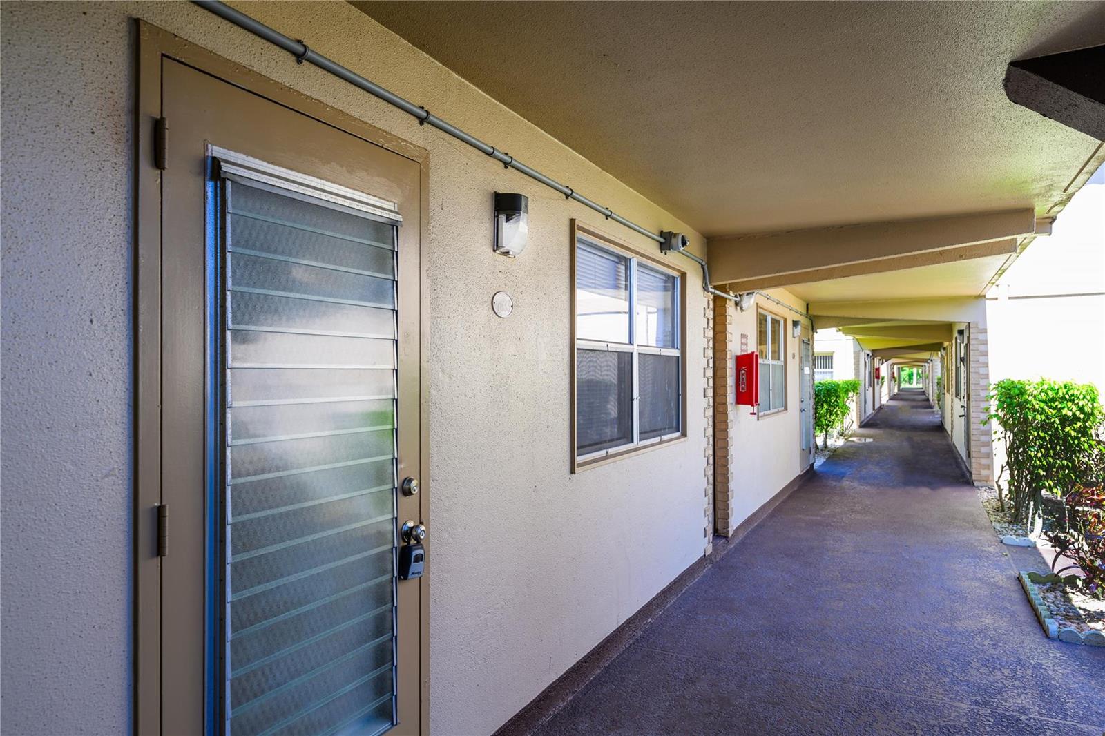 An exterior view of an apartment building walkway with a door, window, and fire extinguisher — 633 Brittany # 633, Delray Beach FL 33446, DELRAY BEACH, FL