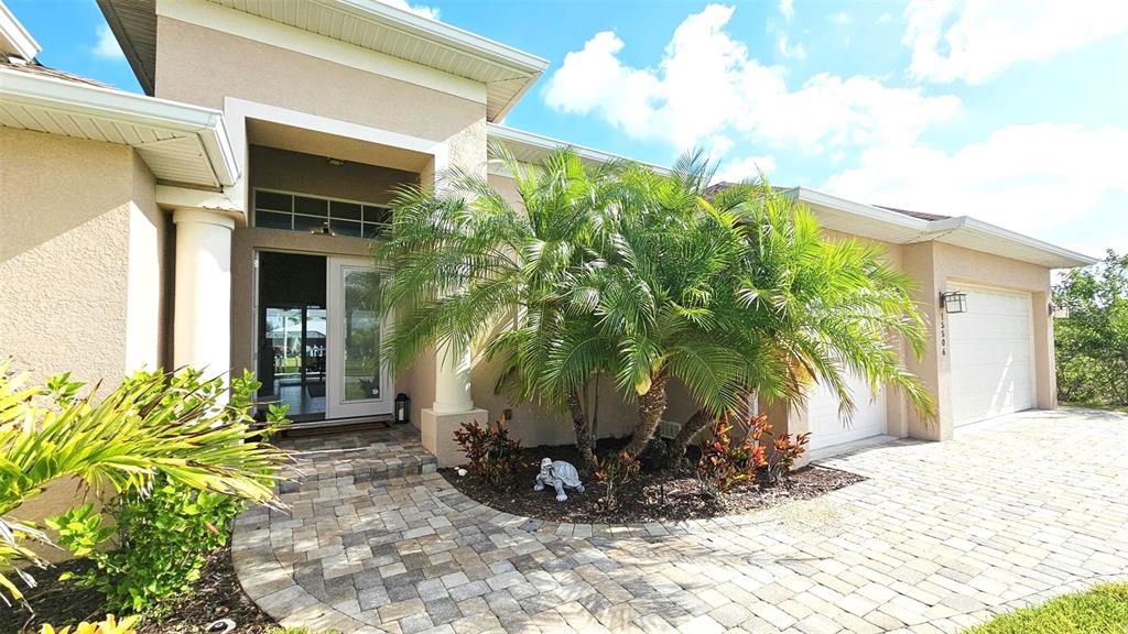 A beige house features a paver driveway, a palm tree, and a covered front entryway — 15506 MEACHAM CIRCLE, PORT CHARLOTTE, FL