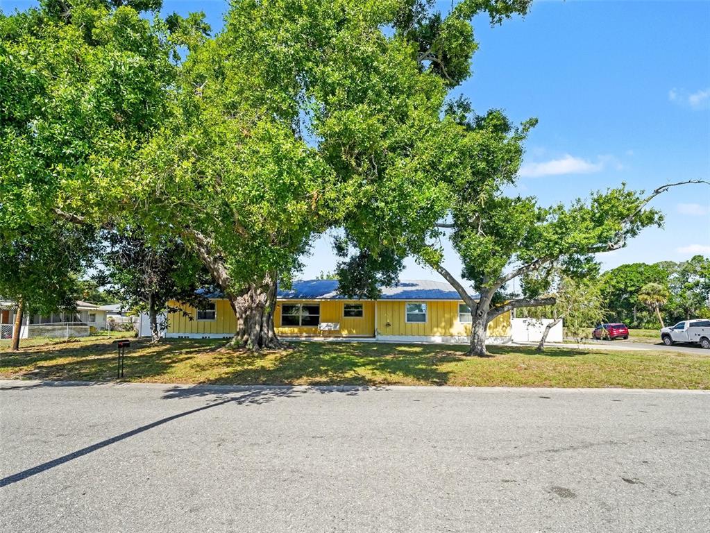 A yellow, single-story house is partially obscured by large, mature trees in the front yard — 704 S LOCKWOOD RIDGE ROAD, SARASOTA, FL