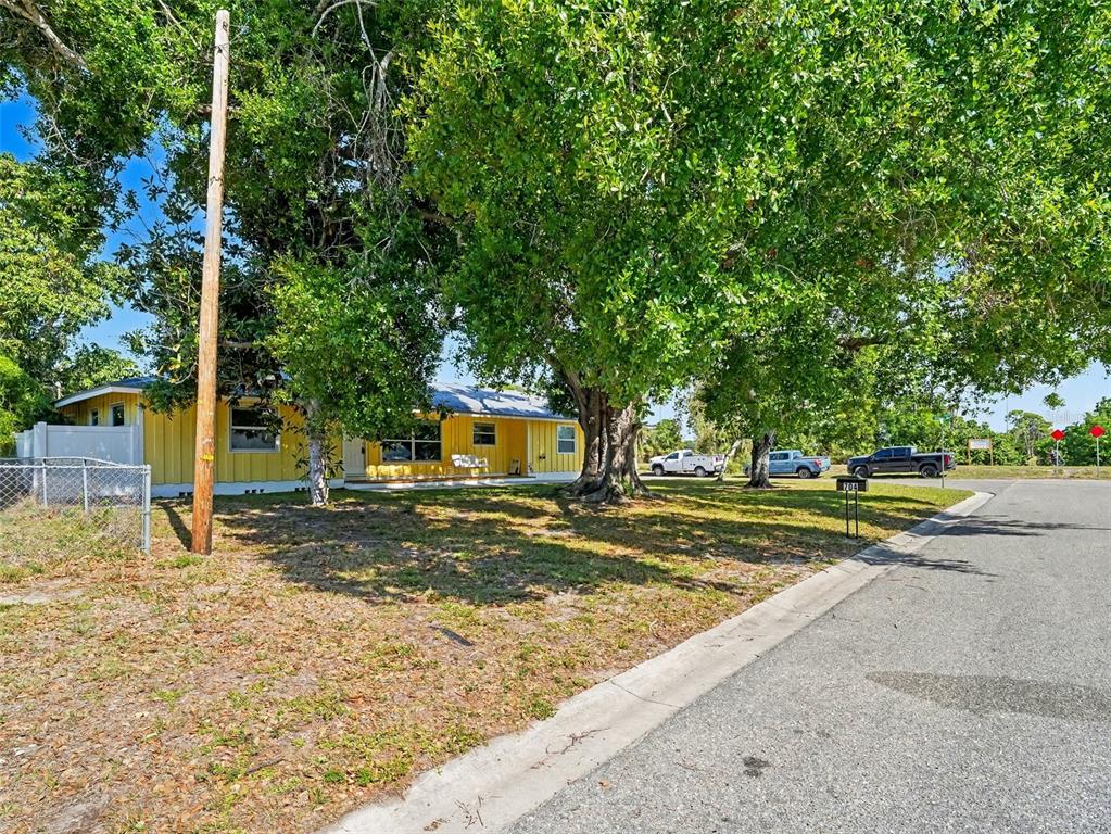 A yellow single-story house sits behind a large tree on a grassy corner lot — 704 S LOCKWOOD RIDGE ROAD, SARASOTA, FL